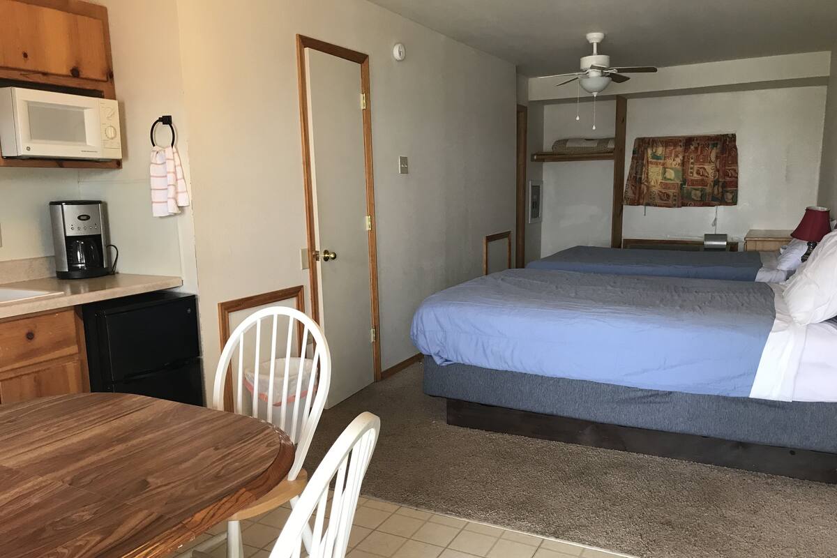 A hotel room with a bed, a desk, a chair, a microwave, a coffee maker, and a ceiling fan.