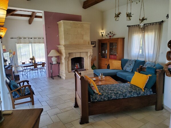 A living room with a fireplace, a sofa, a dining area, and a kitchen visible in the background. - PROMO VILLA NEAR AJACCIO WITH SPA, NEAR BEACHES 5 MIN, 14 PEOPLE / 2 BATHROOM (Afa)
