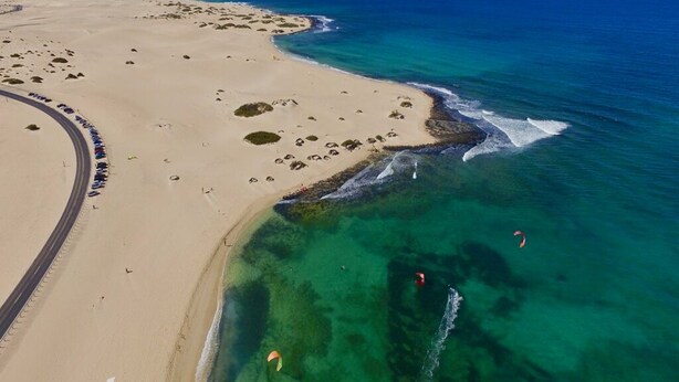 An aerial view of a coastal area with a sandy beach, clear blue waters, and a road curving along the coast. - Semi-detached house in a quiet location for visiting Fuerteventura  (Caldereta)