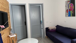 A modern living room with a dark blue sofa, a white coffee table, and a TV mounted on a wooden wall. There are two grey doors and a colorful abstract painting on the wall. - Semi-detached house in a quiet location for visiting Fuerteventura  (Caldereta)