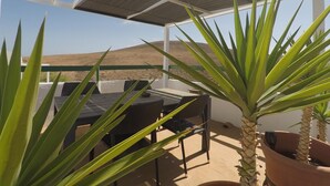 An outdoor patio with a table and chairs, surrounded by potted plants and a view of the landscape. - Semi-detached house in a quiet location for visiting Fuerteventura  (Caldereta)