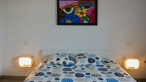 A bedroom with a bed, patterned bedding, a wall-mounted painting, and bedside lamps. - Semi-detached house in a quiet location for visiting Fuerteventura  (Caldereta)