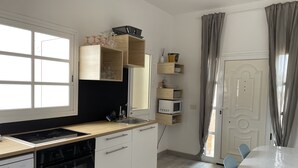 A modern kitchen with a built-in oven, a sink, and wooden cabinets. There is a dining table with chairs and a window with curtains. - Semi-detached house in a quiet location for visiting Fuerteventura  (Caldereta)