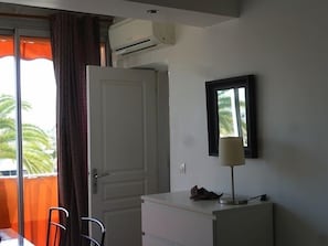 Ett rum med en stängd dörr, ett litet bord med en stol, en lampa och en luftkonditioneringsanläggning på väggen.