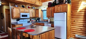 Una cocina con gabinetes de madera, microondas, estufa, lavabo y refrigerador.