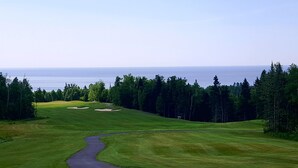 A golf course with a winding path, sand bunkers, and dense forest.