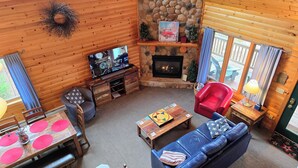A cozy cabin interior with a stone fireplace, wooden walls, a television, a blue sofa, and a dining area.