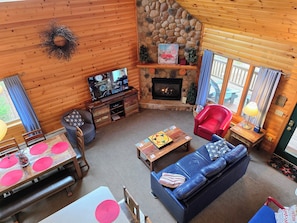 A cozy cabin interior with a stone fireplace, wooden walls, a television, a blue sofa, and a dining area. - Comfortable 3 Bedroom, 2 Bath Cabin Between Lutsen Mountains and Lake Superior (Lutsen)