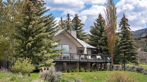 Una casa moderna con una terraza amplia, rodeada de altos árboles y un paisaje cubierto de césped.