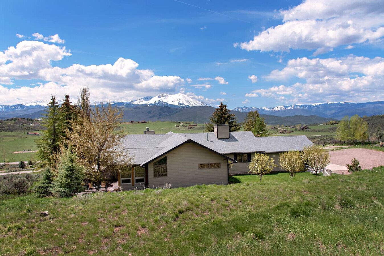 Ein zweistöckiges Haus mit großer Garage und überdachtem Außenbereich, umgeben von einer grünen Landschaft und Bergen im Hintergrund.