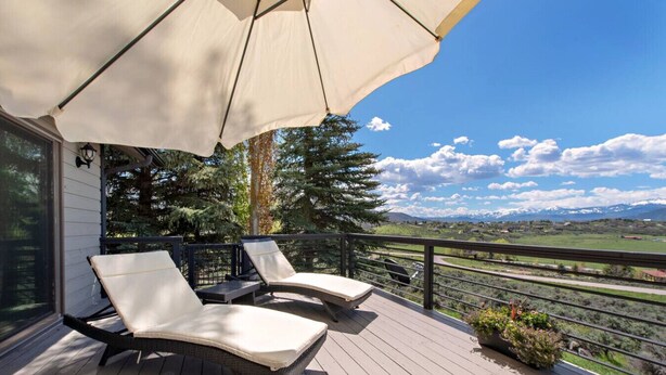 Una terraza con dos sillones de descanso bajo un toldo, con vista a un paisaje pintoresco con montañas y cielo despejado.