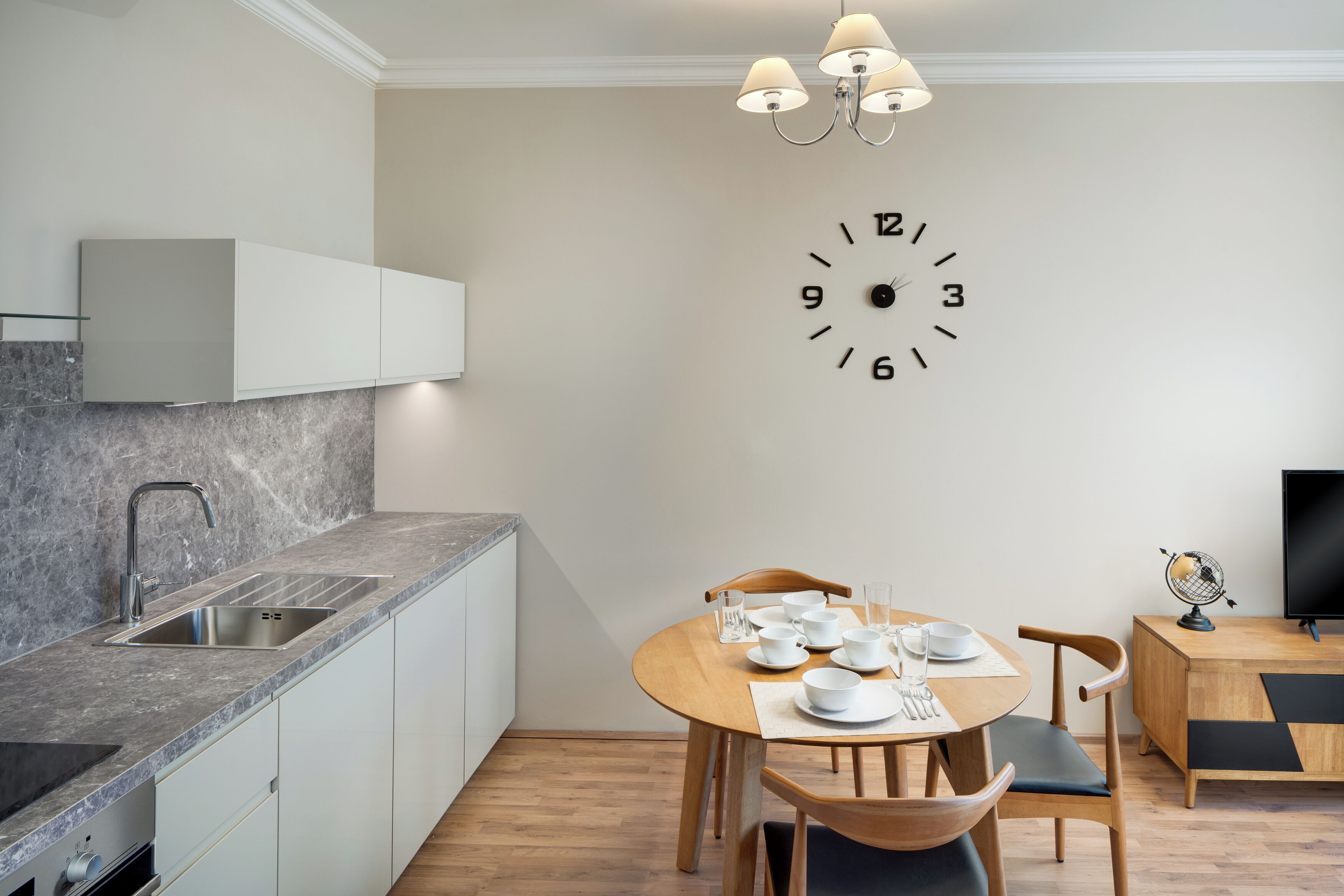 Een moderne keuken met een inbouwspoelbak, een eettafel gedekt met wit servies en een wandklok.