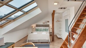 A modern bedroom with a skylight, a bed with pillows, a wooden bench, a table, and a staircase. - Louren Apartments (Prague)