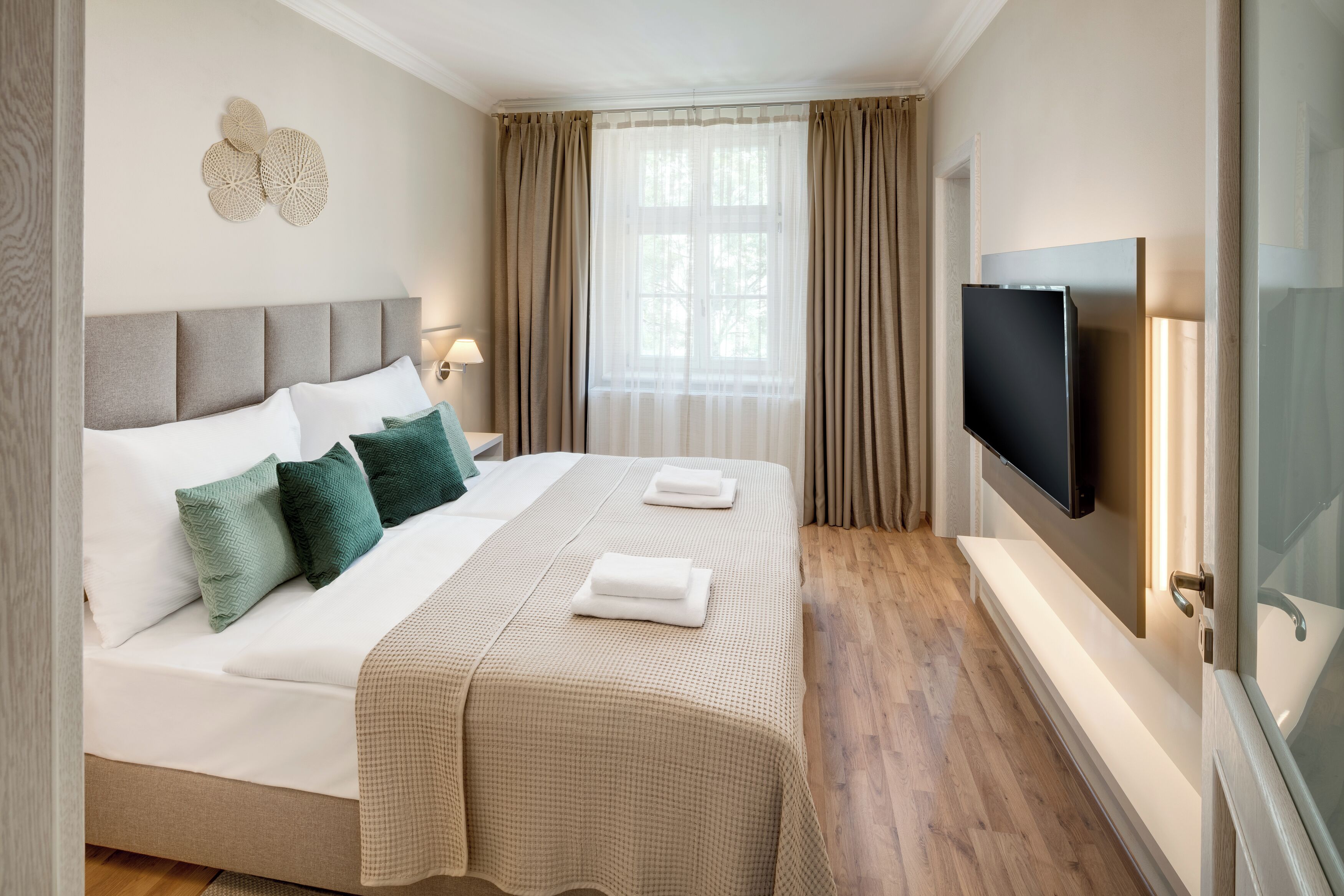 Ett hotellrum med en stor säng, en platt-TV som är monterad på väggen och ett fönster med gardiner.