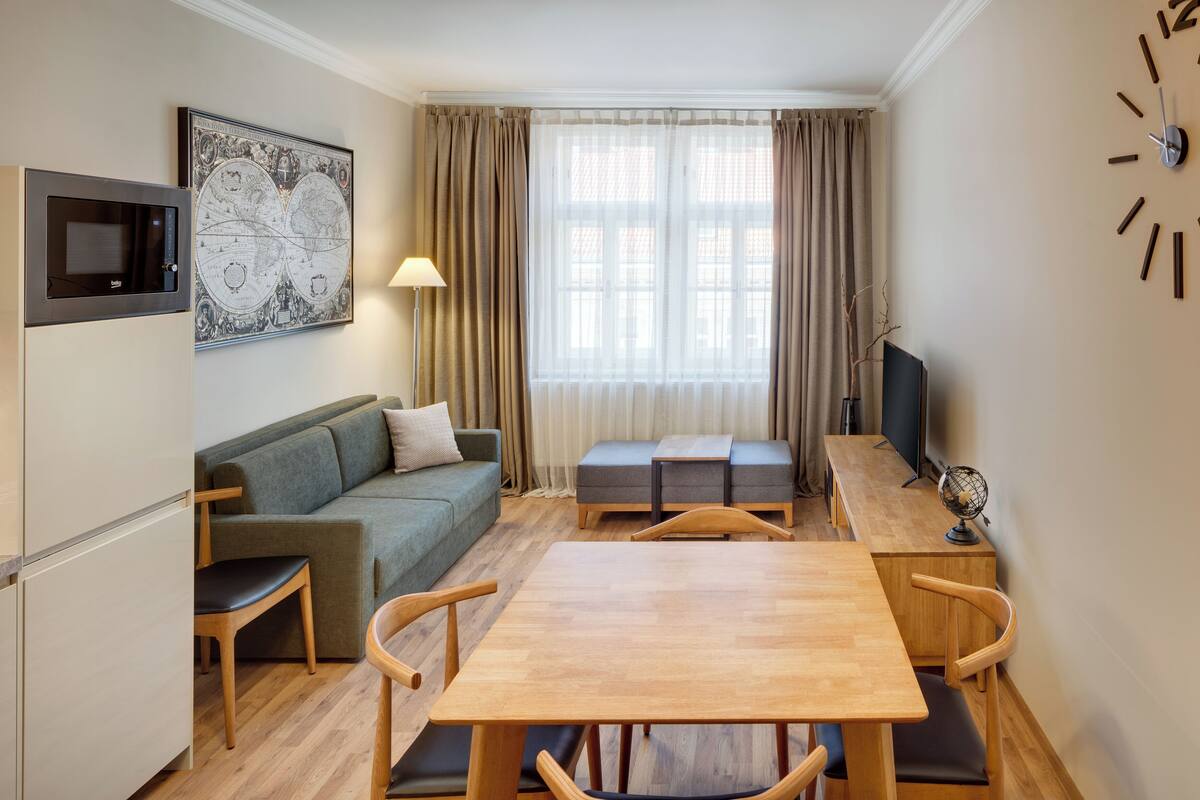 A compact living space with a wooden dining table, two chairs, a sofa, a small bench, a TV, a globe, a lamp, and a world map on the wall.