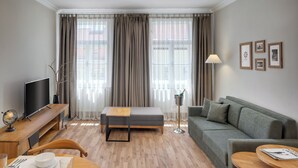 A modern living room with a sofa, a dining table set, a TV, and a lamp. - Louren Apartments (Prague)