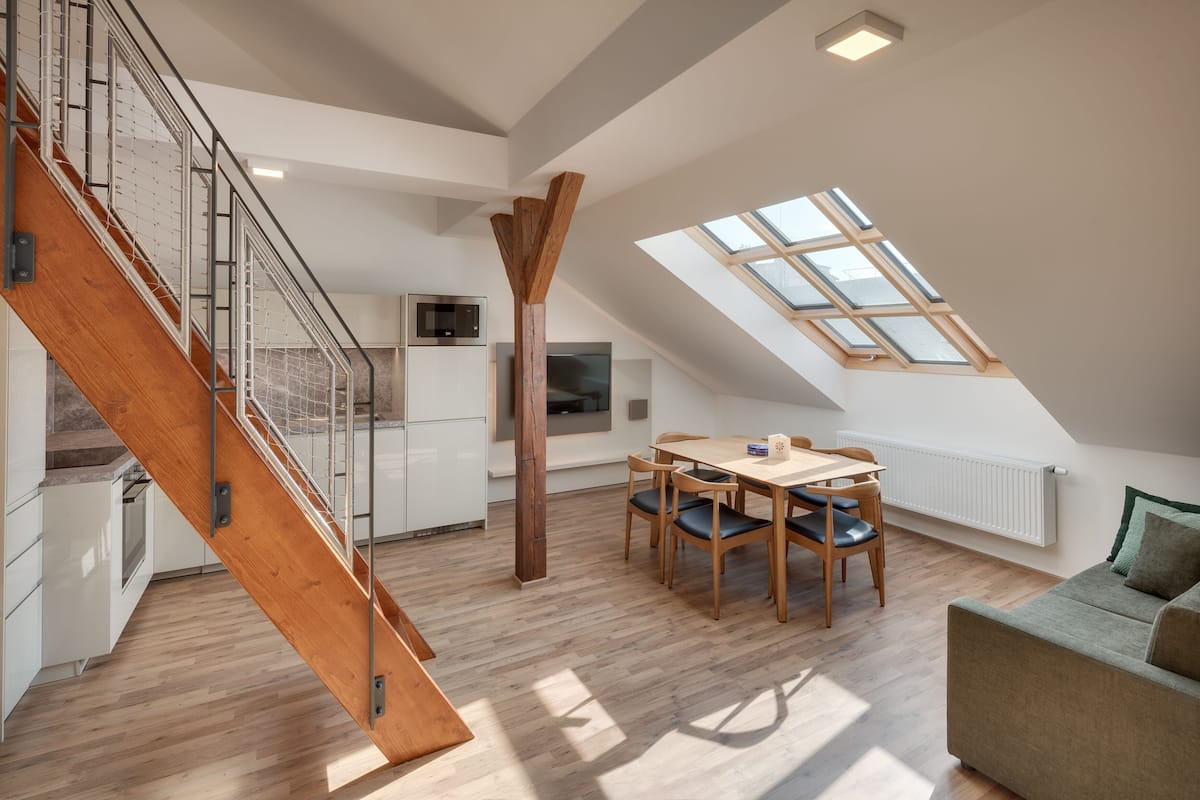 A modern loft with a wooden staircase, a dining area, and a skylight.