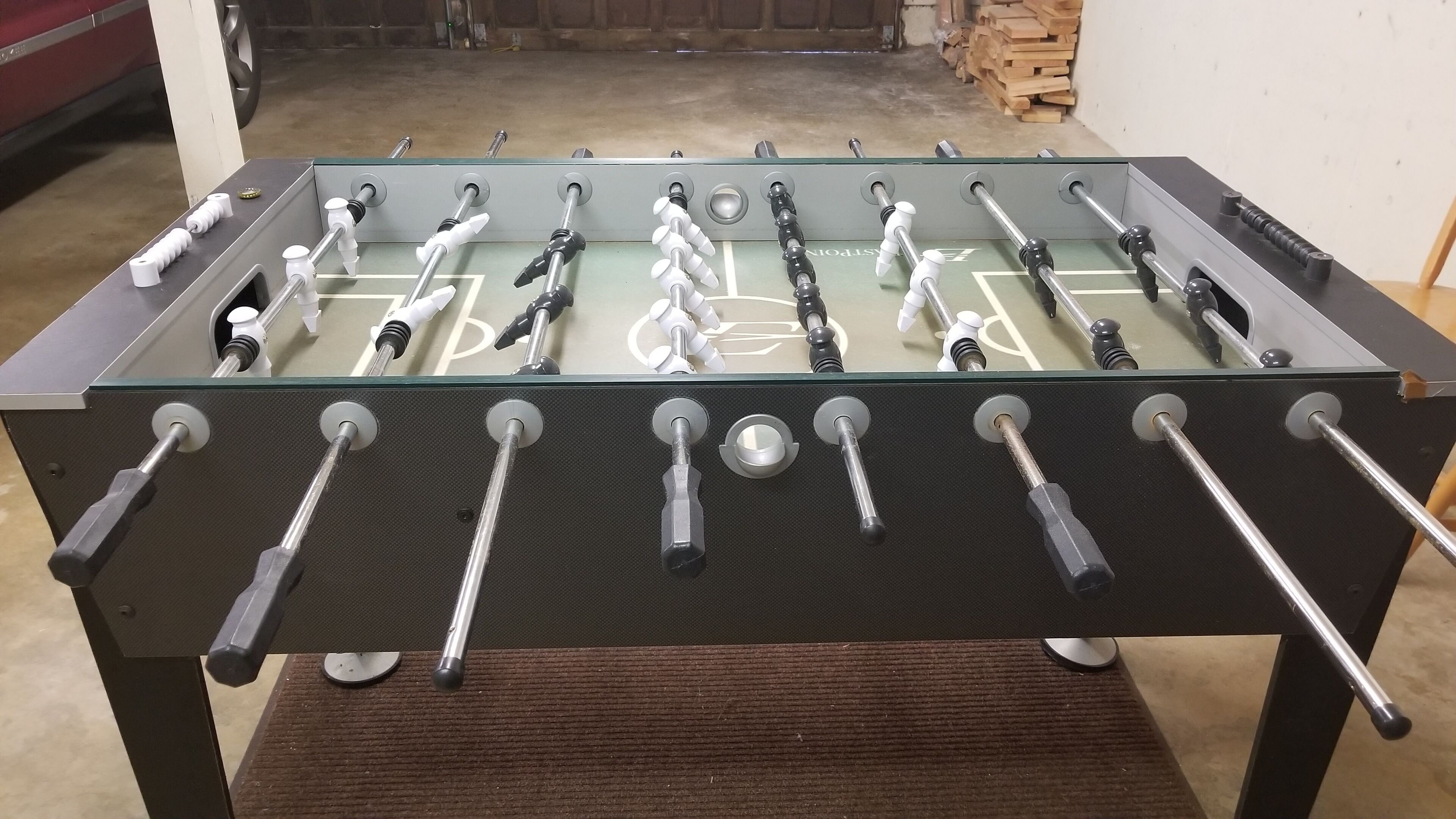 A foosball table with multiple rods and handles, set on a dark, textured surface.