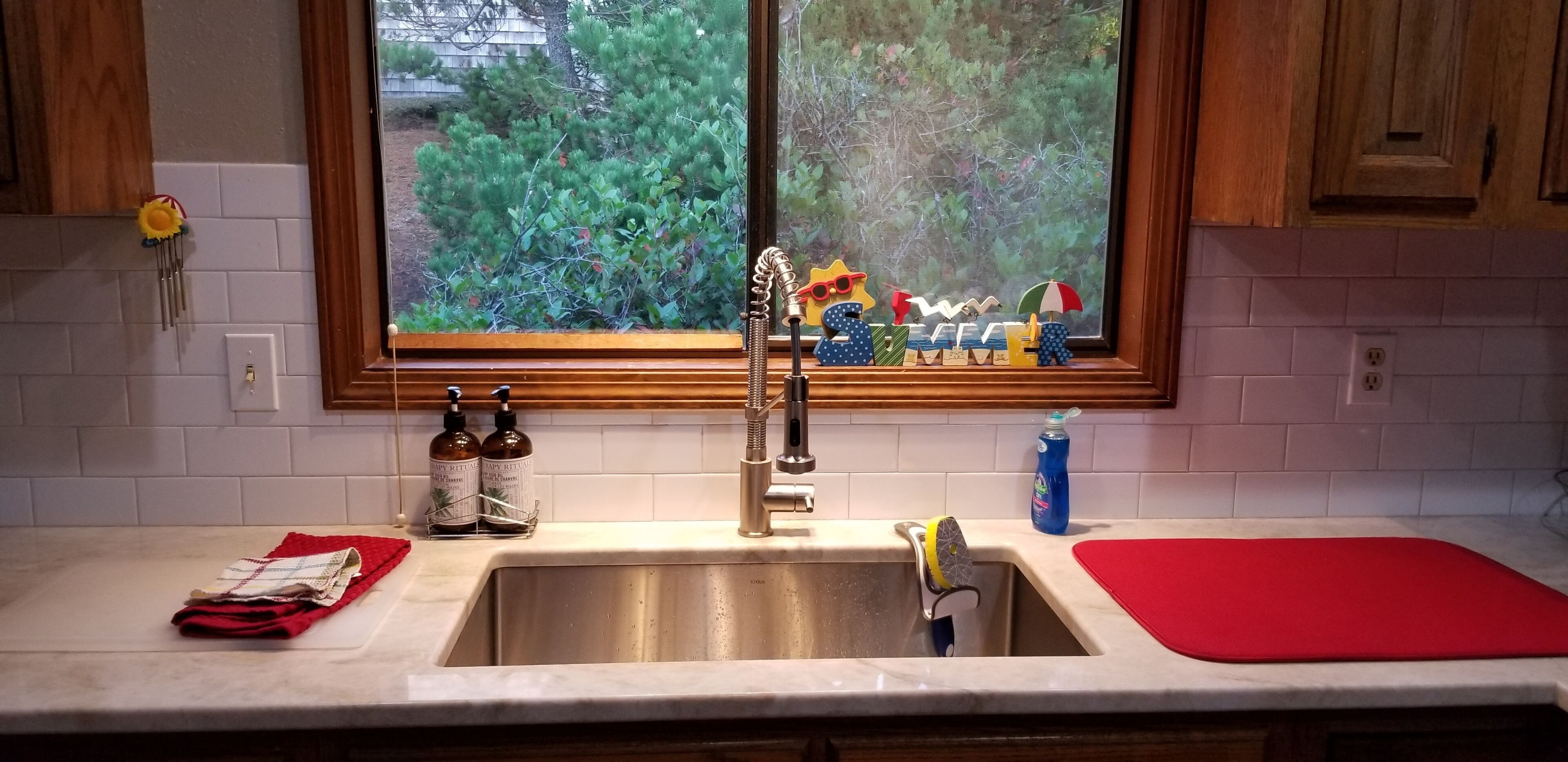 Une cuisine avec une fenêtre, un évier et un tapis rouge sur le plan de travail.