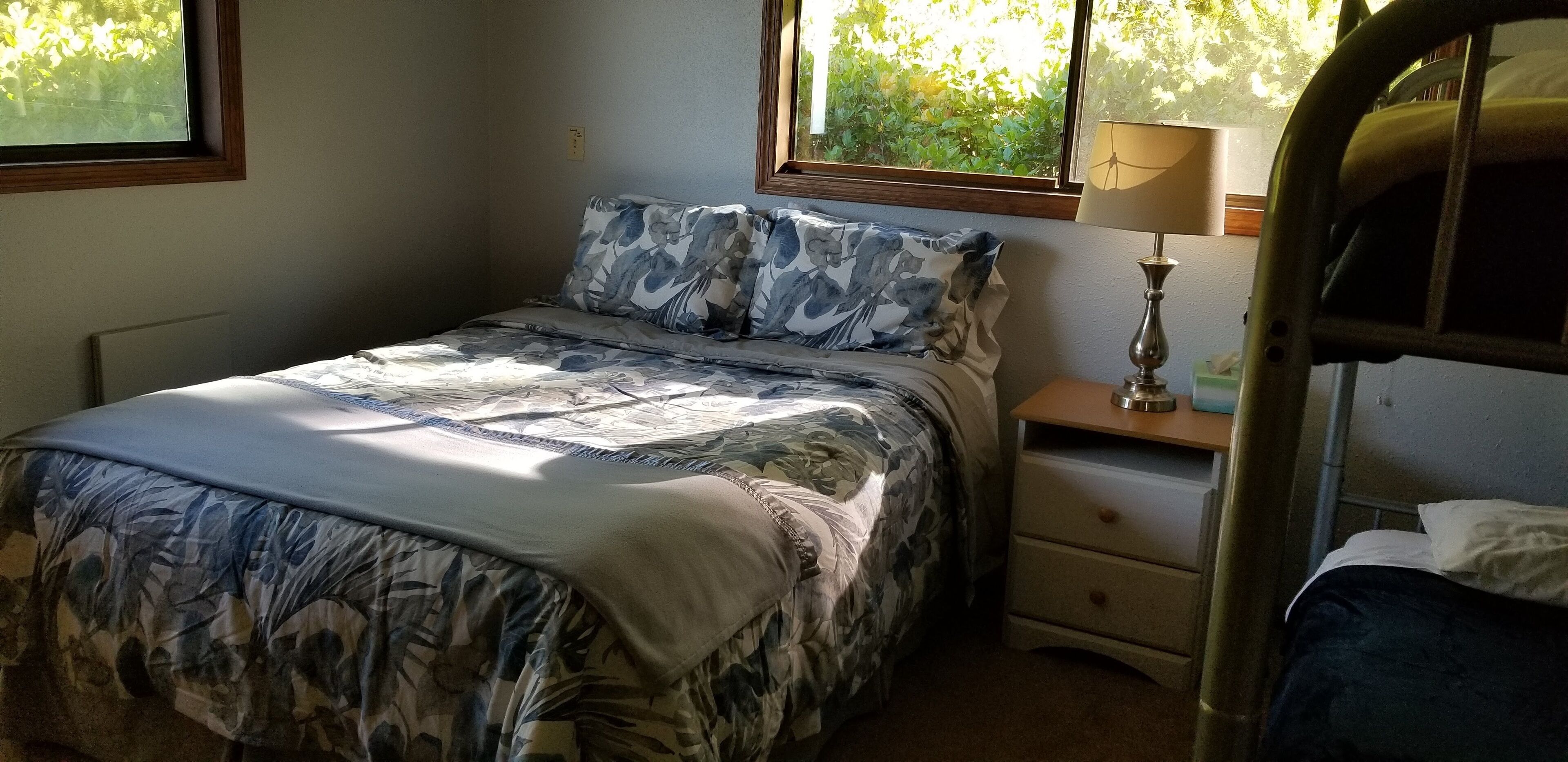 Une chambre à coucher avec un lit, une table de chevet, une lampe et une fenêtre donnant sur un paysage verdoyant.