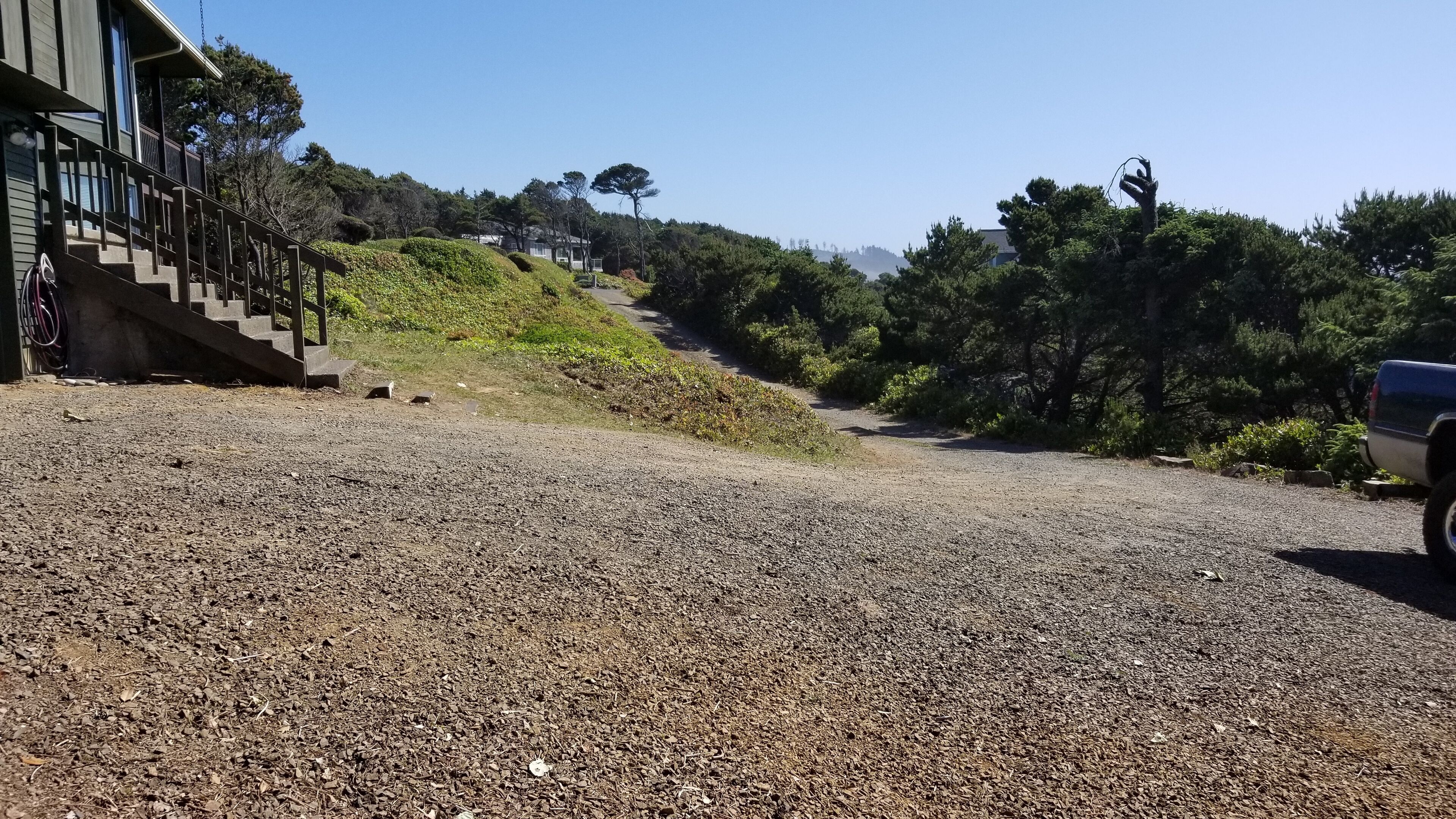 A gravel driveway leading to a house with a wooden staircase and a parked vehicle.