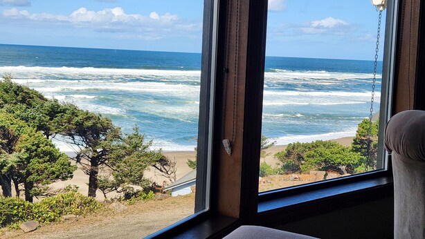 A view of the ocean through a window, with a beach and trees visible outside. - 180 degree ocean beach view. Depoe Bay Lincoln beach area.
quick walk to beach 
 (Lincoln Beach)
