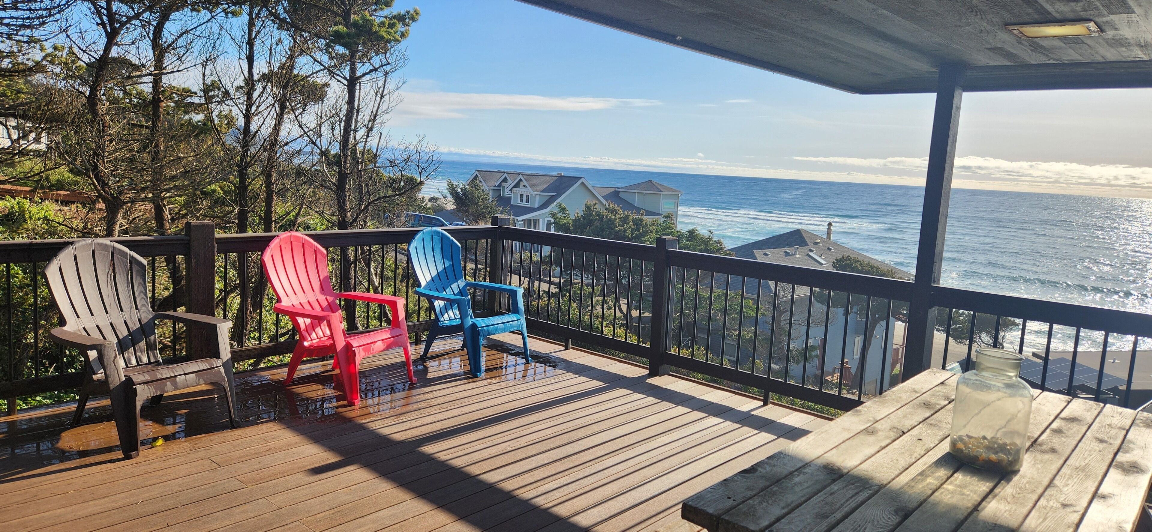 Una terraza de madera con sillas Adirondack, un tarro de cristal y vistas al océano.