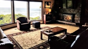 A living room with a large window overlooking a scenic view, a fireplace, and comfortable seating. - 180 degree ocean beach view. Depoe Bay Lincoln beach area.
quick walk to beach 
 (Lincoln Beach)