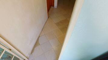Un pasillo estrecho con suelo de baldosas, una puerta de madera y una pared blanca.