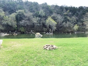 A grassy area with a small pile of rocks in the foreground and a body of water in the background.