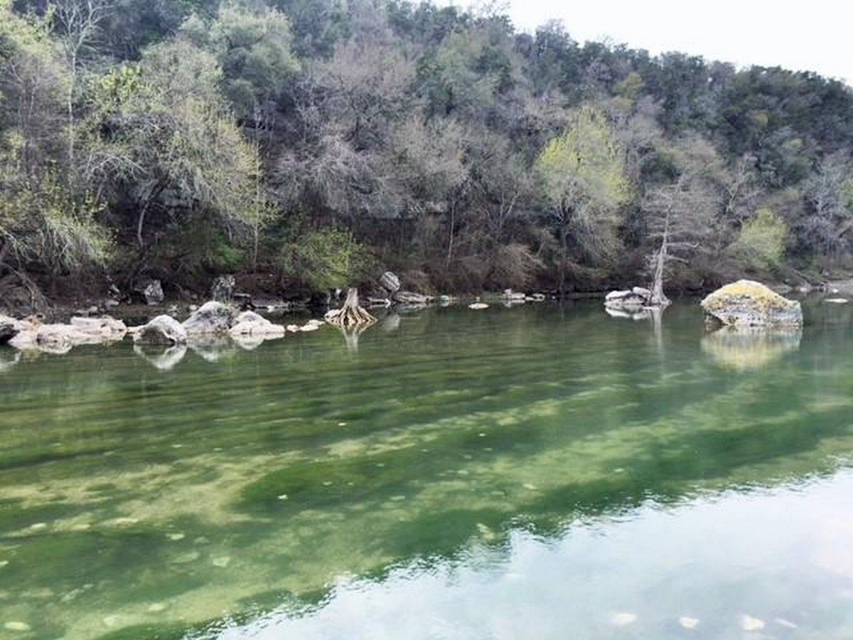 Ein ruhiger Fluss mit klarem Wasser, umgeben von dichtem Wald und felsigem Gelände.