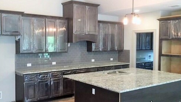 A modern kitchen with dark wooden cabinets, a granite countertop, and a central island.
