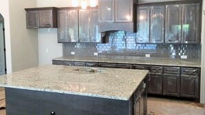 A kitchen with dark cabinetry, a granite countertop, and a three-light fixture above the island.