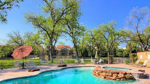 A swimming pool with clear blue water, surrounded by lounge chairs and a red umbrella. - 5 O'Clock Somewhere! WWH302 Apartment 2 New (New Braunfels)