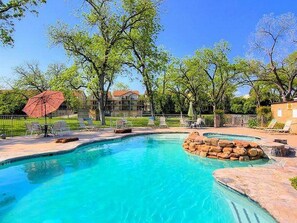 A swimming pool with clear blue water, surrounded by lounge chairs and a red umbrella. - 5 O'Clock Somewhere! WWH302 Apartment 2 New (New Braunfels)