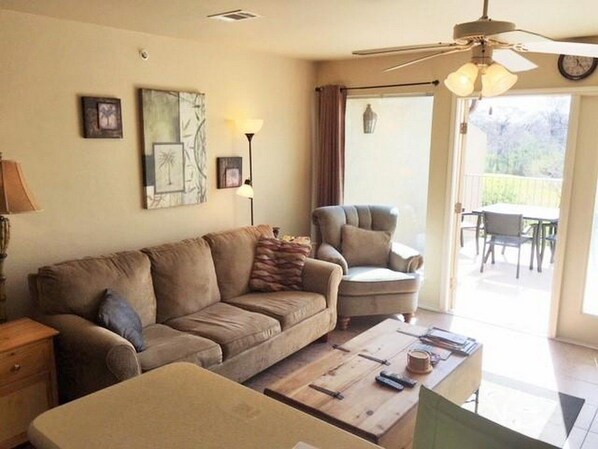 A living room with a sofa, armchair, and coffee table. There is a window with curtains, a ceiling fan, and a door leading to an outdoor area. - 5 O'Clock Somewhere! WWH302 Apartment 2 New (New Braunfels)