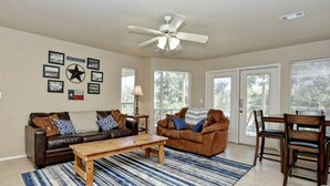 A spacious living room with a large window, a ceiling fan, and a dining area with wooden chairs and a table. - Good Times & Tan Lines WWi201 Apartment 2 New (New Braunfels)