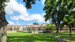 A courtyard with a grassy lawn, a pathway, and a row of buildings with balconies. - Good Times & Tan Lines WWi201 Apartment 2 New (New Braunfels)