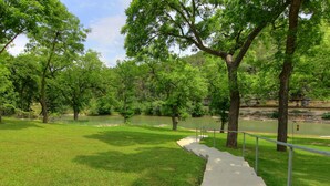 A park with a concrete pathway, trees, and a body of water. - Guadalupe Bluffs RG 304 Apartment 3 New (New Braunfels)