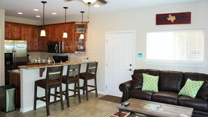 A modern kitchen with wooden cabinets, a central island with bar stools, a refrigerator, and a ceiling fan. - Guadalupe Bluffs RG 304 Apartment 3 New (New Braunfels)