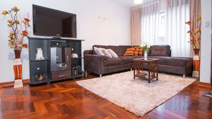 Una sala de estar con un sofá modular, un televisor de pantalla plana, una mesita y jarrones decorativos.