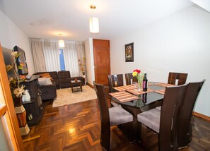 Un comedor con mesa de vidrio, sillas marrones y piso de madera.