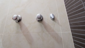 Un baño con suelo de baldosas, un estante metálico y tres grifos.