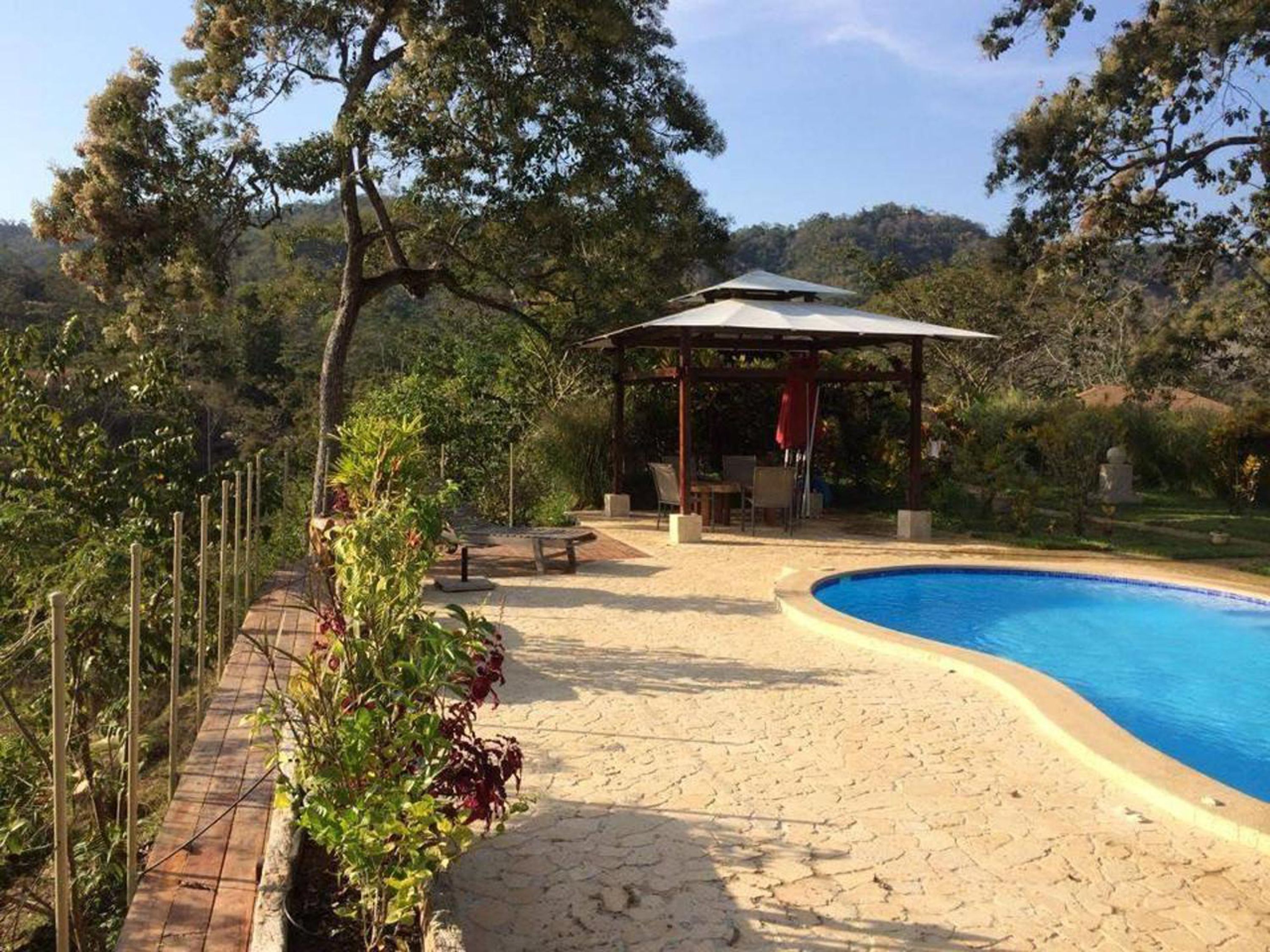 Un área de piscina con muelle de madera, zona de estar cubierta y pérgola.