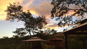 A pool area with a gazebo, surrounded by trees and a sunset view. - Lodge Margouillat (Paquera)