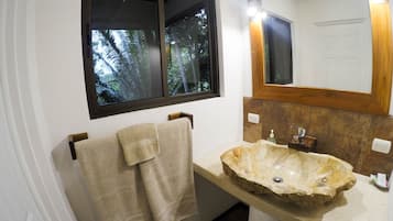 A bathroom with a stone sink, a wooden-framed mirror, and a window with a view of trees.