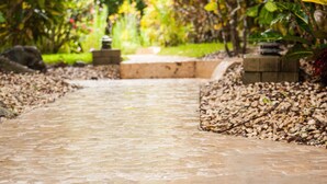 A stone pathway leading through a garden with a water feature and stone steps. - Lodge Margouillat (Paquera)