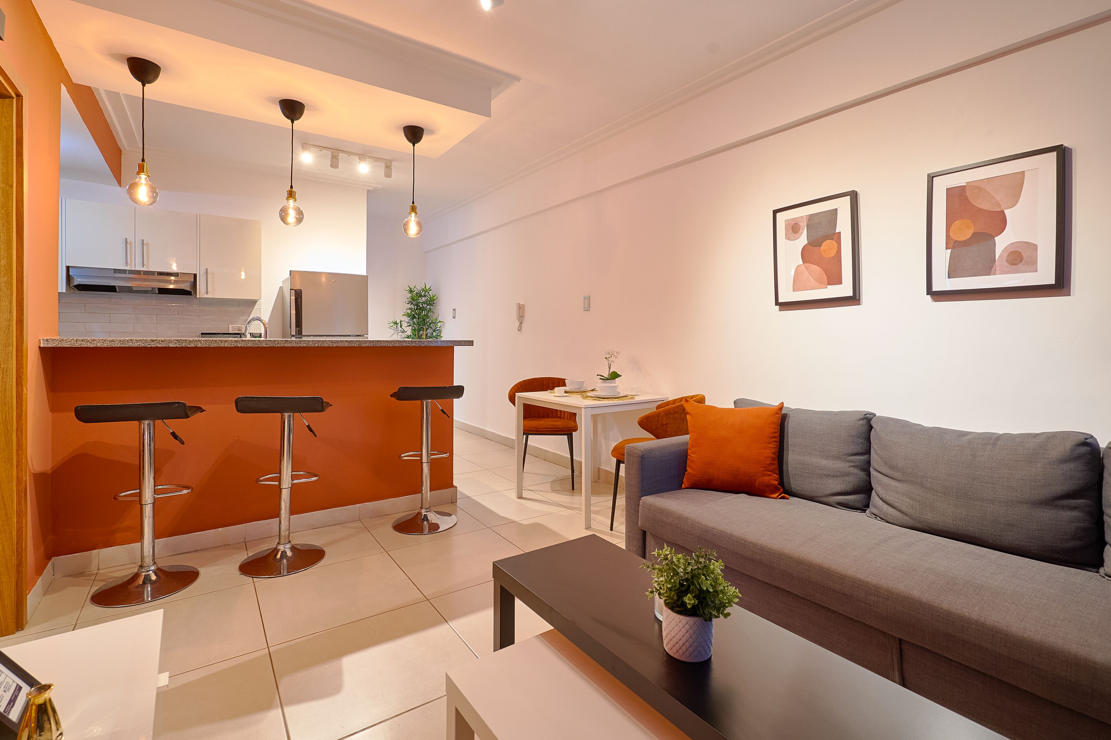 Una sala de estar moderna con un sofá gris, una mesa de centro y un área de cocina con un taburete de bar.