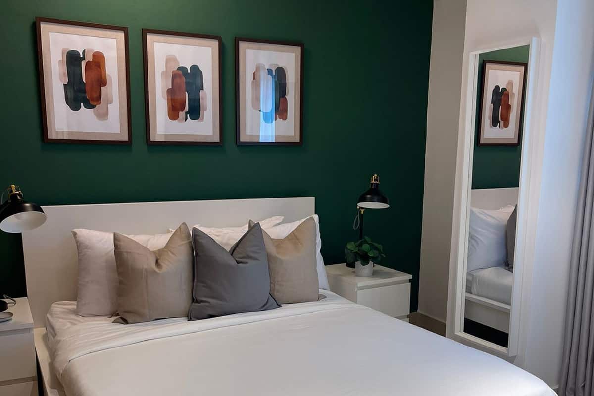 Een moderne slaapkamer met een groot bed, groene wanden en drie ingelijste kunstwerken erboven.