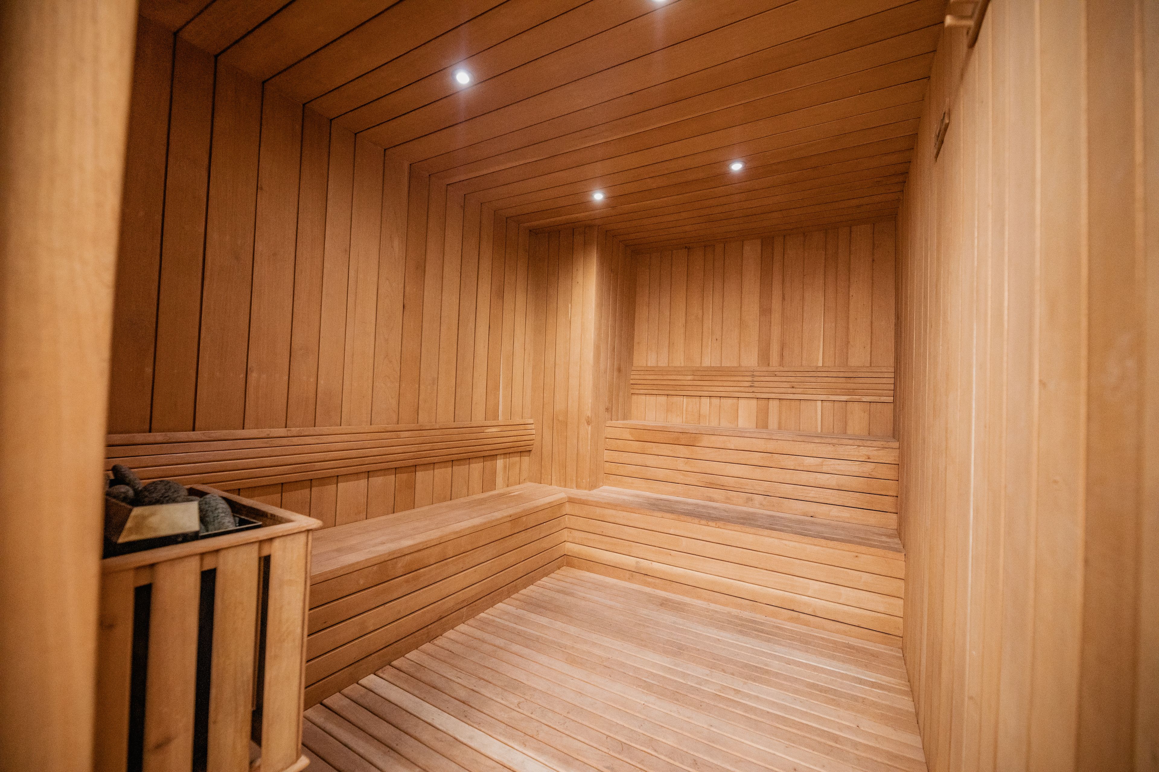 A wooden sauna with benches and a bench with a basket of items.